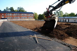 Ein Bagger nimmt Bauarbeiten auf einem Gelände mit einer Schule vor.