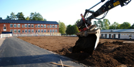Ein Bagger nimmt Bauarbeiten auf einem Gelände mit einer Schule vor.