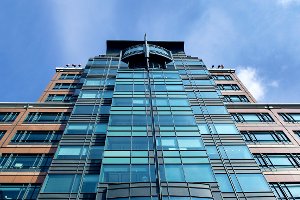 Gläsernes Bürogebäude, von unten gesehen, dahinter blauer Himmel