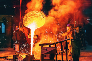 Arbeiter kippt flüssiges Metall aus einem Industriekessel.