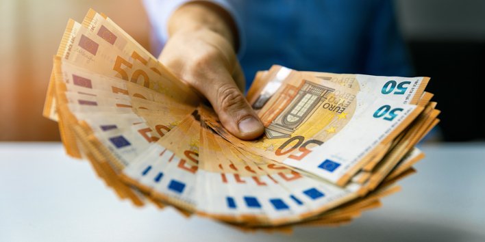 Männerhand hält Fächer von Fünfzigeuroscheinen entgegen.