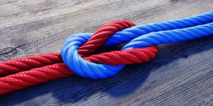 Kreuzknoten mit rotem und blauem Seil auf Holz.