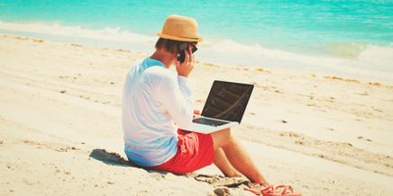 Mann mit Laptop und Handy arbeitet am Strand